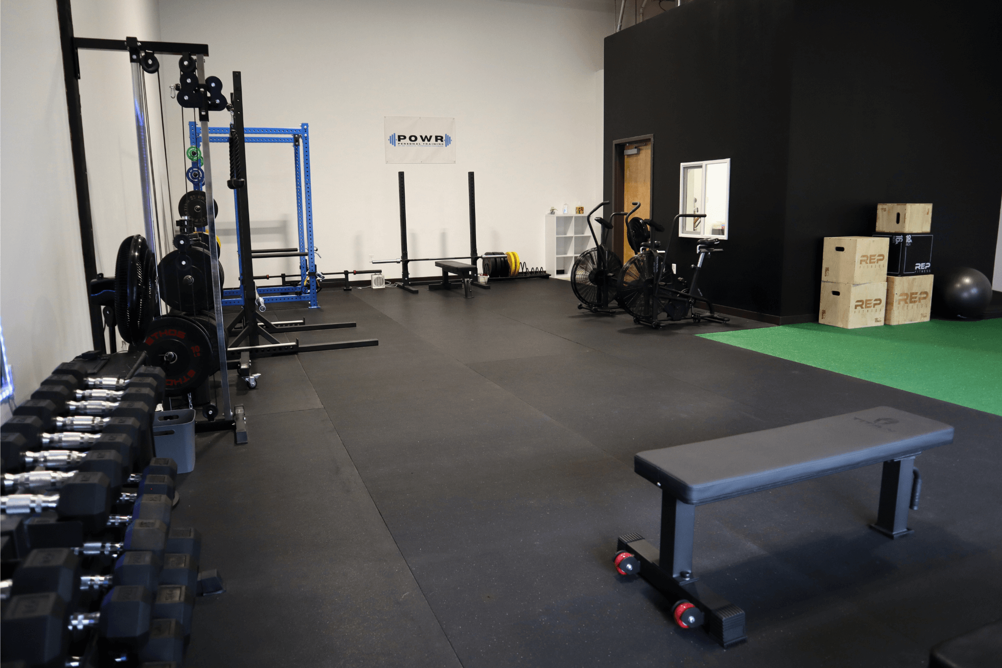 The POWR studio training floor with racks, dumbbells, and a blue power rack